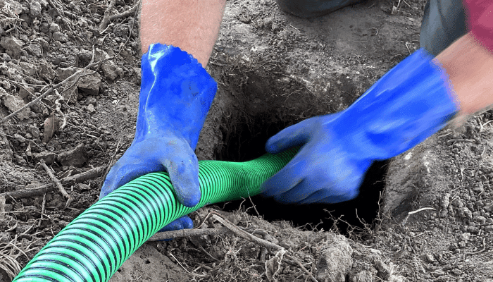 “C&M Plumbing and Septic technician inserting a green hose into the ground during a residential septic inspection in Eastern North Carolina.